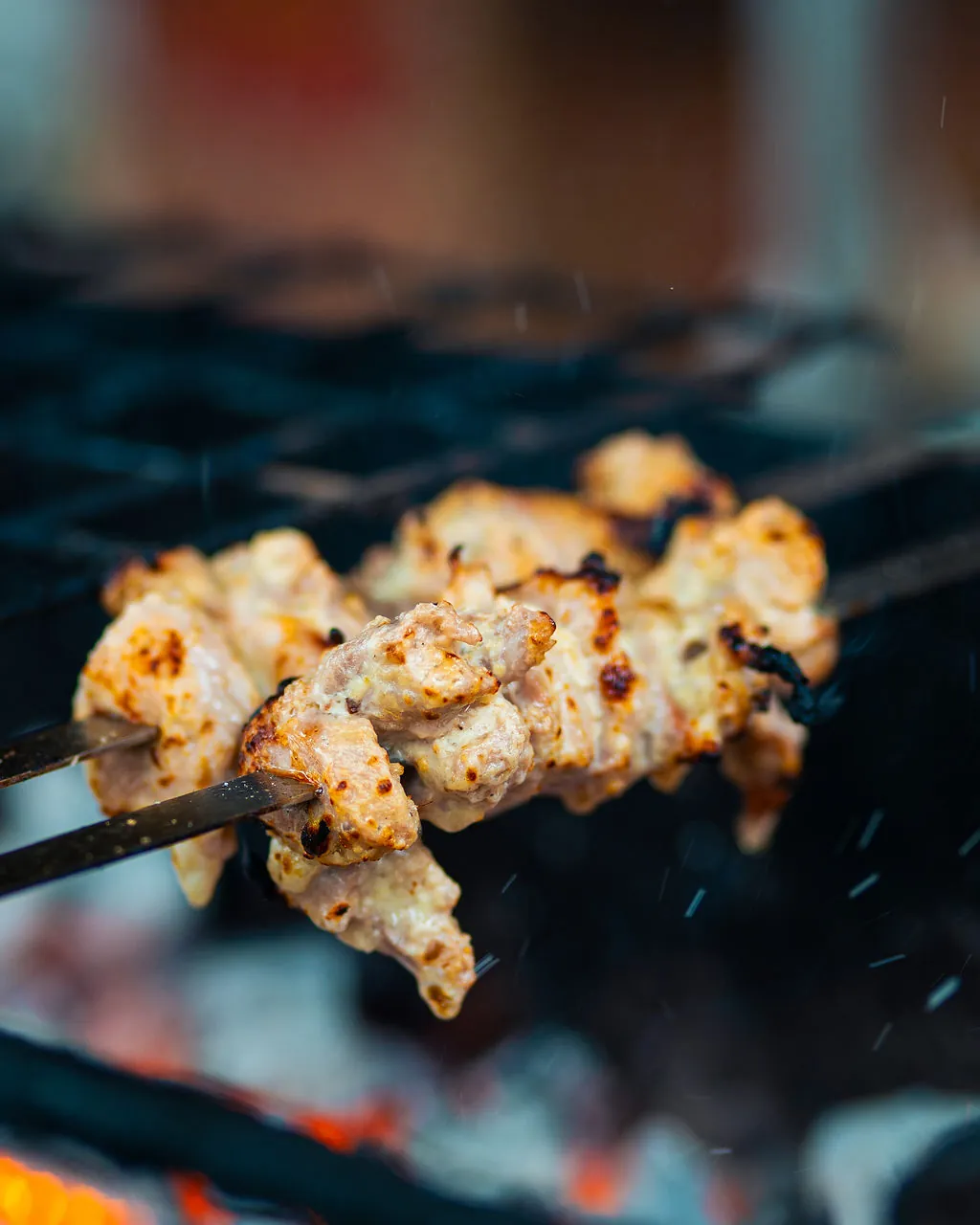 A malai tikka skewer lifted fresh off the charcoal grill over glowing embers at Kaka's Barbecue